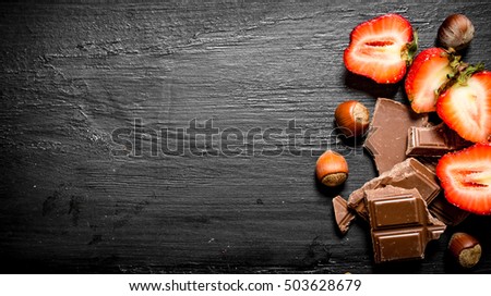 Strawberries with slices of chocolate and nuts. On the black wooden table.