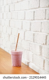 Strawberries smoothie with eco straw in biodegradable plastic glass on the table next to white brick wall