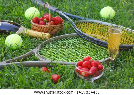 Strawberries with whipped cream, glass with champagne and tennis rackets and balls on grass. Wimbledon Grand slam tennis concept. 