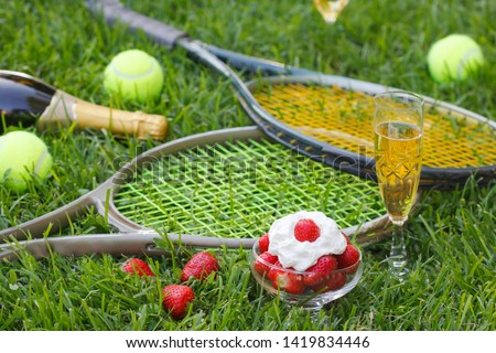 Strawberries with whipped cream, glass with champagne and tennis equipment on Wimbledon tournament grass. Wimbledon Grand slam celebration concept. 