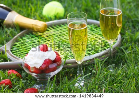Strawberries with whipped cream, glasses with champagne and tennis equipment on Wimbledon tournament grass. Wimbledon Grand slam celebration concept. 