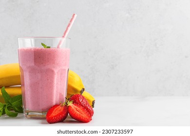 Strawberry and banana smoothie or milkshake in a glass with straw, fresh berries and mint on white background