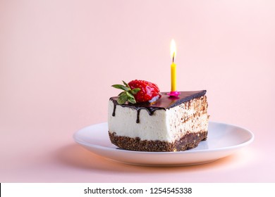 Strawberry cake with cream, dripping chocolate glaze and a lit candle in a plate on a pink background for birthday and holiday celebrations. Make a wish and blow out the candle on the birthday cake - Powered by Shutterstock