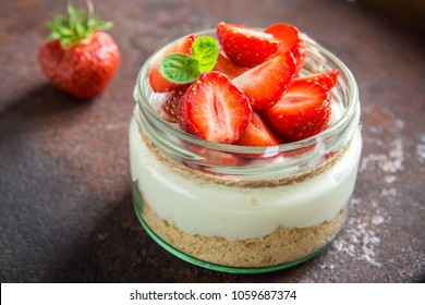 Strawberry cheesecake in glass jar with fresh strawberries and cream cheese  on dark background. Healthy homemade dessert.