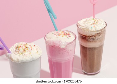 Strawberry, chocolate and vanilla milkshake with whipped cream on pink background. Place for text. Sweet drinks