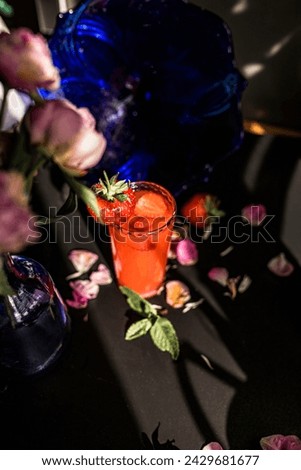 Strawberry cocktail in a glass on a black background with flowers. Freshness and vibrancy concept