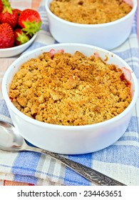 Strawberry crumble in a white bowl with a spoon on blue napkin on linen tablecloth background