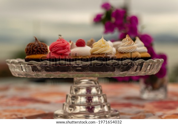 strawberry cupcake, chocolate cupcake,\
vanilla cupcake and cream cupcake on a table seen from above. sweet\
breakfast, several cupcakes in a glass holder\
outdoors