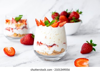 Strawberry dessert with white cocolate, whipped cream, granola and fresh strawberry in individual trifles glass on marble. Recipe of simple healthy homemade organic dessert, cheesecake, parfait.