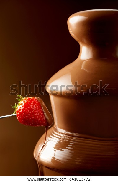 Strawberry dipped in\
chocolate from a fondue fountain dripping sauce in a close up view\
with copy space\
behind