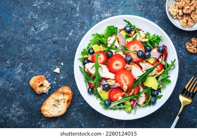 Strawberry, grilled chicken and herbs healthy salad with arugula, blueberries, avocado and walnuts, blue kitchen table. Fresh useful dish for healthy eating - Powered by Shutterstock