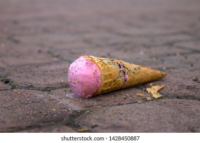 Strawberry Ice Cream Falling On A Street Sidewalk And A Broken Waffle Cone