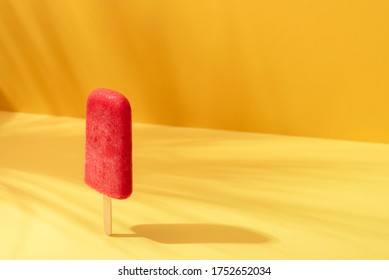 Strawberry ice cream popsicle on a yellow background in sunlight. Cooling dessert. Red sorbet on a stick. Sunny tropical summer context.