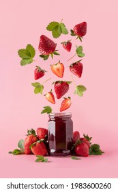 Strawberry jam in glass jar and falling pieces of strawberry. Strawberry Levitation. Levitation berries on a pink background.