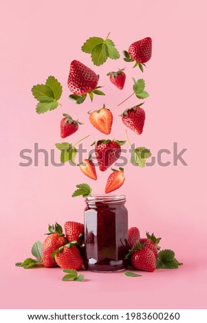 Strawberry jam in glass jar and falling pieces of strawberry. Strawberry Levitation. Levitation berries on a pink background.