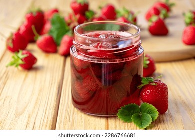 Strawberry jam in glass jar on wooden board with fresh strawberry fruit and green leaves on wooden background. Recipe of delicious homemade berry jam of strawberry full of vitamins and antioxidants.
