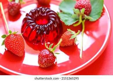 Strawberry jelly.Berry jelly.Low calorie diet dessert.Red jelly and strawberries with green leaves on a red plate on a Red background.Healthy natural sweets and desserts. 