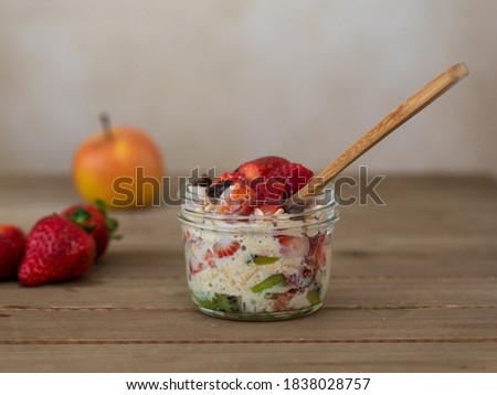 Strawberry and Kiwi overnight oats on brown wooden able with wooden spoon and plenty of copy-space, and an apple in the background - healthy eating concept