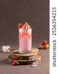 Strawberry Milkshake: A creamy strawberry milkshake topped with whipped cream and fresh strawberries, placed on a rustic board with ice cubes 