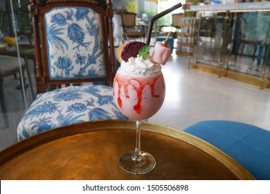 Strawberry MilkShake In Wine Glass With Whipping Cream, Cracker, Dried Dragon Fruit And Marshmallow. Gold Metal Table