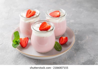 Strawberry mousse in a glass jar on a gray concrete background with whipped cream, fresh berries and mint leaves. Delicious summer dessert