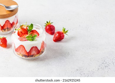 Strawberry parfait with yogurt and granola in a glass jar, copy space. Healthy breakfast recipe. Summer dessert concept.