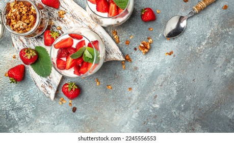 strawberry parfaits with fresh fruit, yogurt and granola on white table, glass jar. Healthy breakfast. Long banner format. top view.