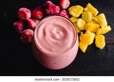 Strawberry Pineapple Smoothie With Frozen Fruit In The Background: A Pink Smoothy Shown With Frozen Strawberries And Pineapple Chunks