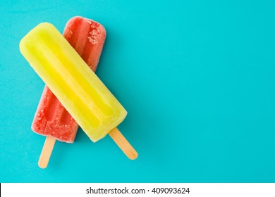 Strawberry popsicle and lemon popsicle on blue background
