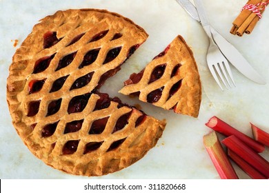 Strawberry and rhubarb pie with cut piece on a marble background, overhead scene