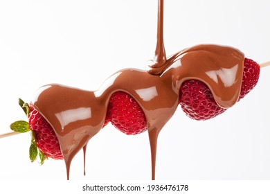 Strawberry skewer with melted milk chocolate being poured isolated in studio with a white background