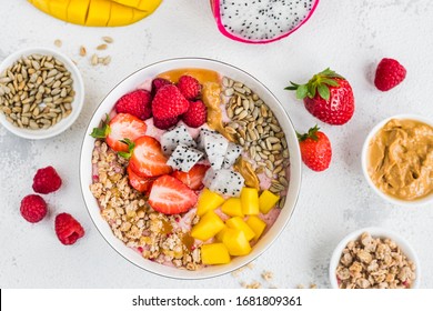 Strawberry Smoothie Bowl With Strawberries, Raspberries, Mango, Dragon Fruit, Granola, Peanut Butter And Sunflower Seeds In A White Plate On A Light Background