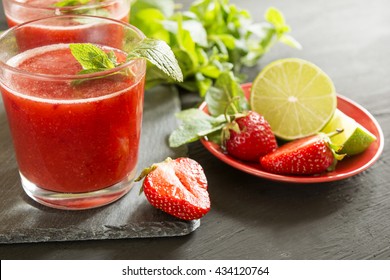 Strawberry Smoothie In A Glass On A Dark Surface On A Background Of Leaves Of Lemon Mint And Lime