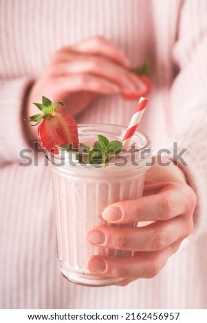 Strawberry smoothie. Vegan smoothie from strawberry, banana, chia seeds and mint in glass in hands of female wearing pink sweater. Clean eating, alkaline diet, weight loss food concept. Mock up.