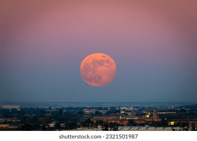 The strawberry Supermoon (Supermoon of strawberry) at sunset gradient from blue to pink on the city skyline in June 2020 in Spain.