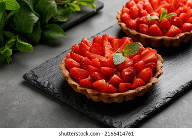 Strawberry Tarts with cream decorated with mint on slate board and dark background. Cake basket with strawberries. Sweet dessert.