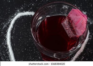 Strawberry Tea And Tea Bag In Glass, Spilled Sugar In Shape Of Heart Around, On Dark Background