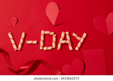 Strawberry wafer roll arranged with the words V-DAY, ribbons and paper hearts on a red background. Love space for advertising. Flat lay, copy space. Loving wishes.