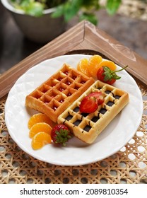 Strawberry Waffel Or Waffle And Chocolate Waffel Of Waffle With Strawberry And Orange Fruits For Topping, Serving In White Plate On Rattan Wicker Table.