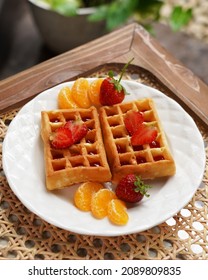 Strawberry Waffel Or Waffle With Strawberry And Orange Fruits For Topping, Serving In White Plate On Rattan Wicker Table.