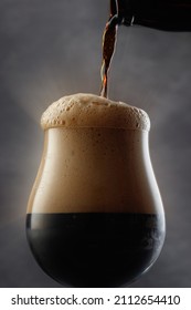 Stream Of Dark Stout Pours Into A Beer Glass. Detail Of Dark Beer With Overflowing Foam Head. Selective Focus	