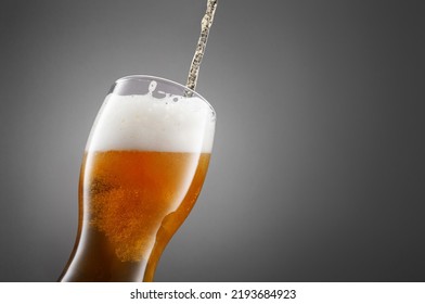 Stream of draught beer in glass on a granite stone. Glass of fresh and cold beer on gray dark background. Selective focus - Shutterstock ID 2193684923