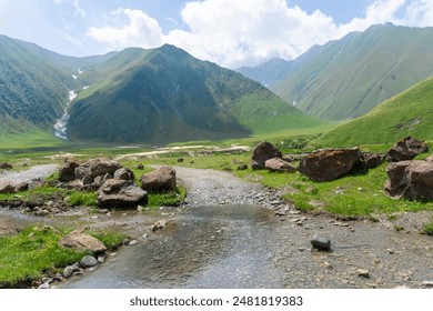 A stream flow crosses a gravel road leading along the river valley to the mountains - Powered by Shutterstock