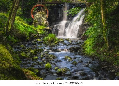 Stream leading to red waterwheel and waterfall in Glenariff Forest Park, County Antrim, Northern Ireland. Long exposure and soft focus photography