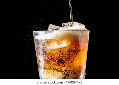 Stream Of Soda Being Pouring Into A Glass With Soda And Ice Cube On Black Background, Closeup Texture, Splashing, Splash, Fizz 