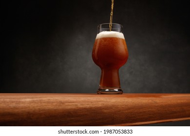 Stream Of Stout Beer Pours Into A Beer Glass On A Bar Counter. Glass Of Beer On Dark  Background. Dark Ale Beer With Foam Head. Selective Focus