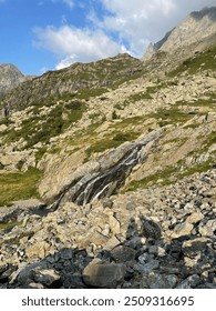 A stream that flows strongly between rocks and meadows that then flows into a river. The water is frozen even in summer.