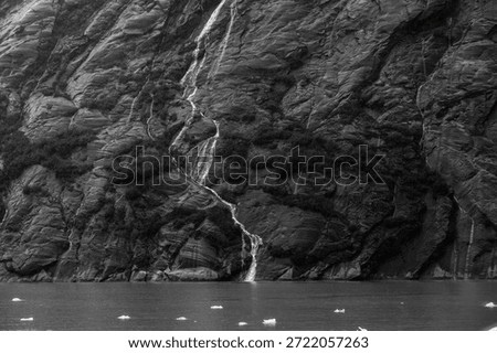 A stream trickles down the stone face of a mountain in the Endicott Fjord in Alaska, contrasted on black and white.