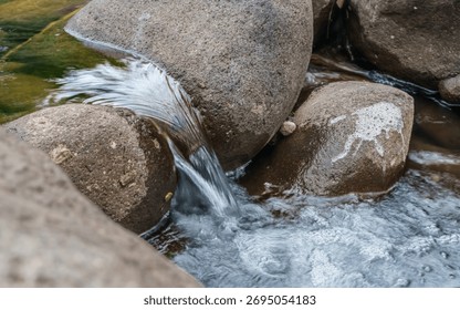 A stream of water is flowing between two large rocks. The water is clear and calm, and the rocks are large and rough. The scene is peaceful and serene