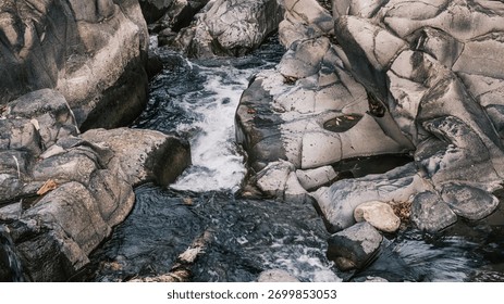 A stream of water flows between large rocks. The water is clear and calm, and the rocks are jagged and rough. The scene is peaceful and serene